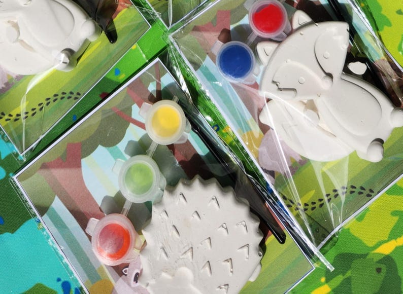 May include: A paint-your-own craft kit featuring three different animal shapes: a hedgehog, a butterfly, and a fox. The kit includes four small pots of paint in red, blue, yellow, and green.