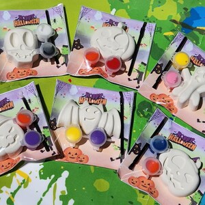 May include: Set of six Halloween-themed paint-your-own ceramic ornaments. Each ornament features a different Halloween character, including a ghost, pumpkin, bat, witch, and two skulls. Each ornament comes with a small paintbrush and three paint pots.
