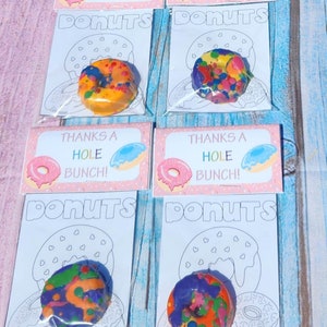 May include: Four clear plastic bags with colorful donut-shaped crayons inside. Each bag has a pink and white card with the text "Thanks a Hole Bunch!" and a donut illustration. The bags are labeled "Donuts".