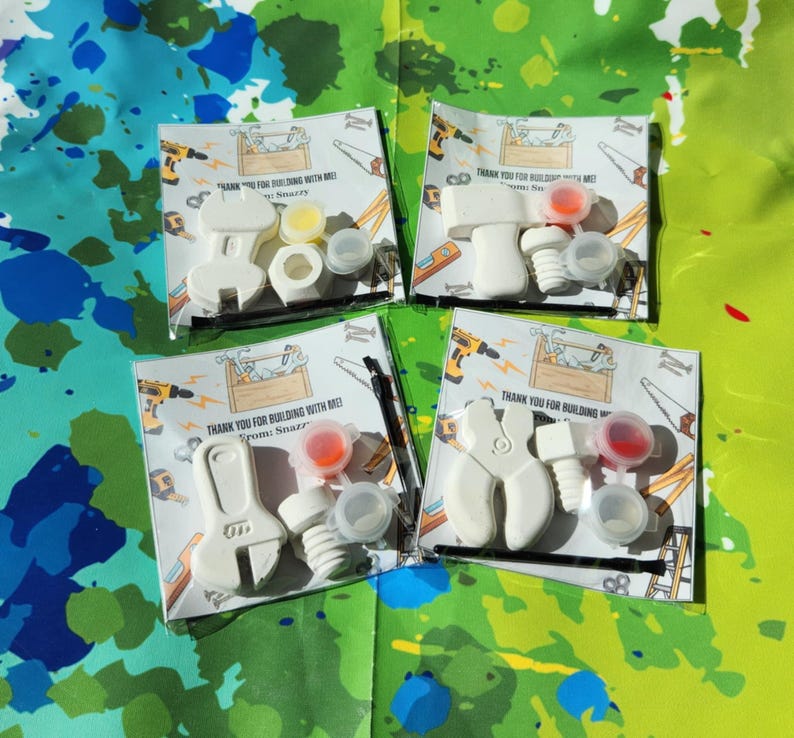 May include: Four white plastic tool-shaped party favours with paint pots and thank you tags. The tags say "Thank you for building with me!" and "From [Name]".