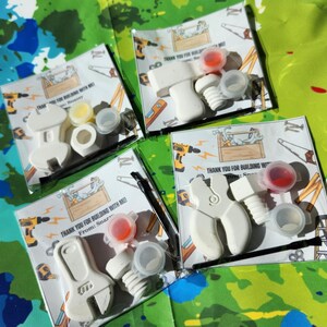 May include: Four small white plastic tool-shaped party favours with paint pots and thank you cards. The cards say "Thank you for building with me! From: Snazzy".