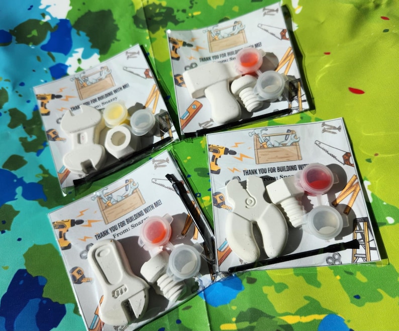 May include: Four small white plastic tool-shaped party favours with paint pots and thank you cards. The cards say "Thank you for building with me! From: Snazzy".