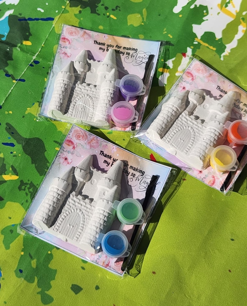 May include: Three sets of DIY castle painting kits. Each kit includes a white castle figurine, two paint pots, and a small paintbrush, all packaged in a clear plastic bag. The text on the card reads "Thank you for making my day so Magic."