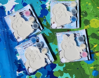 May include: Four paint-your-own penguin kits. Each kit contains a white penguin-shaped figure, small paint pots in various colours, and a paintbrush. The kits are packaged in clear plastic bags with text that reads "Thanks for making much fun!"