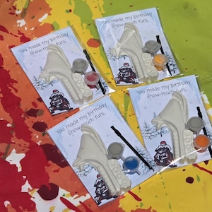May include: Four clear plastic favor bags each containing a white snowmobile-shaped plaster figure, a small black paintbrush, and two small paint pots in varying colors. The backing card features a snowmobile graphic and the text You made my birthday snow-much fun.