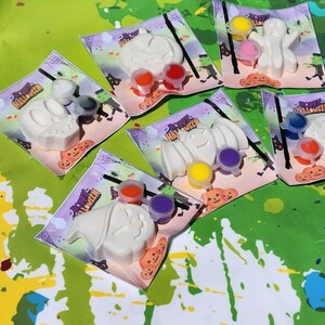 May include: Five Halloween-themed paint-your-own kits with white ceramic figures of a ghost, bat, pumpkin, witch, and skull. Each kit includes paint pots in various colors and a paintbrush.