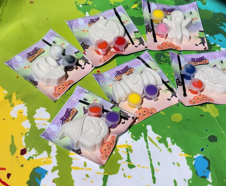 May include: Five Halloween-themed paint-your-own kits with white ceramic figures of a ghost, bat, pumpkin, witch, and skull. Each kit includes paint pots in various colors and a paintbrush.