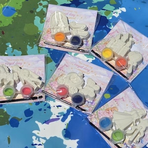 Puede incluir: Cinco kits de manualidades individuales en envases de plástico transparente, cada uno con figuras de yeso blanco, dos pequeños botes de pintura de varios colores y un pincel fino. Las tarjetas llevan el texto You made my royal day magical.