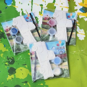 May include: Three paint-by-number kits featuring a white ceramic truck with a blue background. Each kit includes a small paintbrush, a small container of white paint, and three small containers of blue paint.