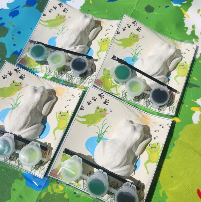 May include: Four sets of frog-shaped ceramic figurines with paint pots and brushes for painting. Each set includes a frog figurine, three paint pots, and a paintbrush. The paint pots are green, light green, and dark blue.
