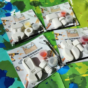 May include: Four favour bags with a white wrench, hammer, and screwdriver, paint, and a thank you note that says "Thank you for building with me! from: Snazz".
