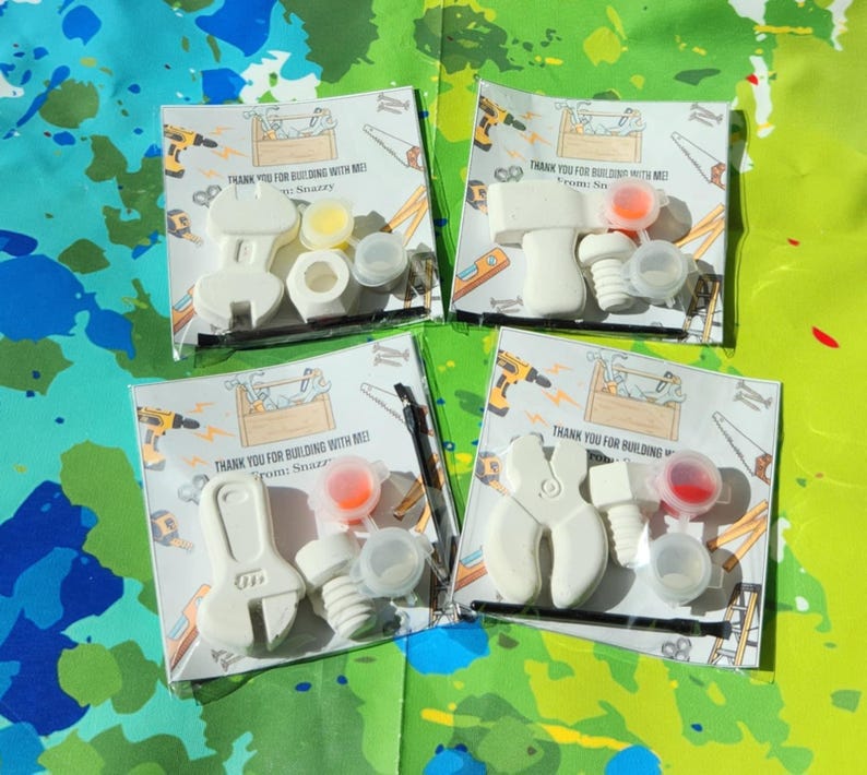 May include: Four small white plastic tool-shaped party favours with paint pots and lids. The favours are packaged in clear plastic bags with printed thank you cards. The cards say "Thank you for building with me!" and "From Snazzy".