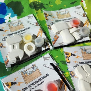 May include: Thank you for building with me! Party favour bags with a white plastic tool, paint, and a thank you note. The note says "Thank you for building with me! From: Snazzy".
