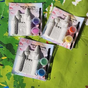 May include: Three castle-shaped plaster craft kits, each packaged with paint pots and a paintbrush. The kits include a card with the text "Thank you for making my birthday so Magic". The paint colors are pink, purple, orange, yellow, green, and blue.