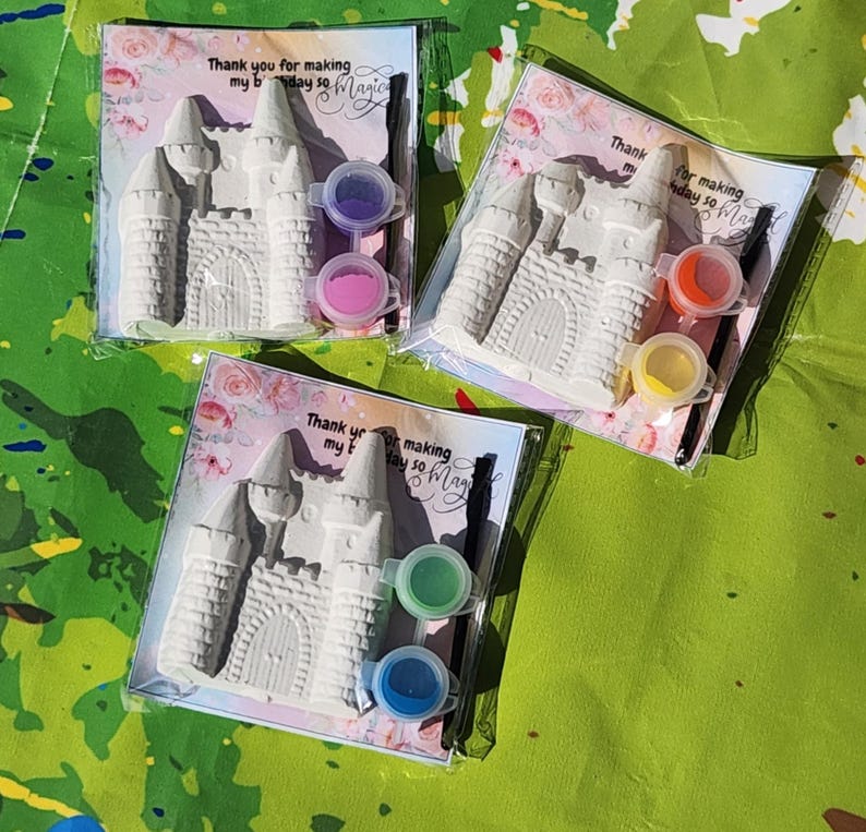 May include: Three castle-shaped plaster craft kits, each packaged with paint pots and a paintbrush. The kits include a card with the text "Thank you for making my birthday so Magic". The paint colors are pink, purple, orange, yellow, green, and blue.