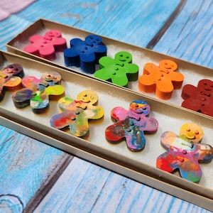 May include: A set of eight colorful gingerbread man crayons in two cardboard boxes. The crayons are arranged in rows and are ready for use.
