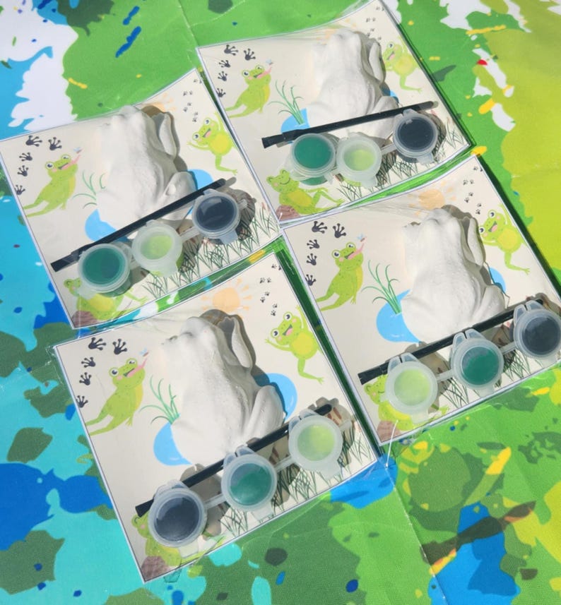 May include: Four white ceramic frog figurines with green paint pots and paintbrushes. Each frog is on a card with a green frog illustration and the words "Froggy Fun".