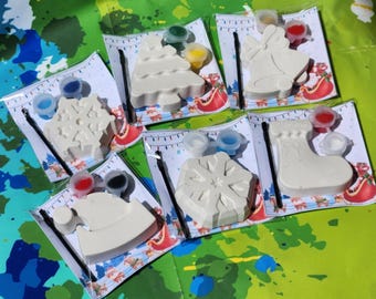 May include: Six Christmas-themed paint-your-own ceramic ornaments. The ornaments include a stocking, a snowflake, a Christmas tree, a Santa hat, a bell, and a snowflake. Each ornament comes with a paintbrush and a set of paint pots.