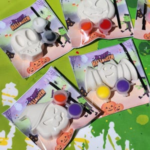 May include: A set of four Halloween-themed paint-your-own kits. Each kit includes a white ceramic figurine, a small paintbrush, and three small pots of paint. The figurines are a skull, a pumpkin, a bat, and a ghost. The kits are packaged in clear plastic bags with a Happy Halloween label.