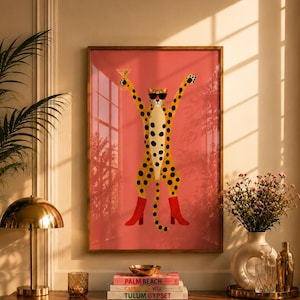 May include: A framed wall art print featuring a stylised yellow leopard with black spots, wearing black sunglasses and bright red boots, holding a martini glass against a solid coral pink background, displayed in a wooden frame.
