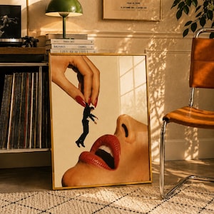 Könnte beinhalten: Ein rechteckiger Kunstdruck in einem dünnen goldenen Rahmen mit einer surrealistischen Collage. Das Bild zeigt eine große Hand mit roten Fingernägeln, die eine kleine Figur im schwarzen Anzug über geöffneten Lippen mit rotem Lippenstift hält.