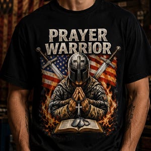 Puede incluir: Una camiseta negra con el texto PRAYER WARRIOR sobre un gráfico de una figura con casco y equipo táctico rezando sobre un libro abierto con un collar de cruz, dos espadas cruzadas y una bandera estadounidense rodeada de llamas naranjas.