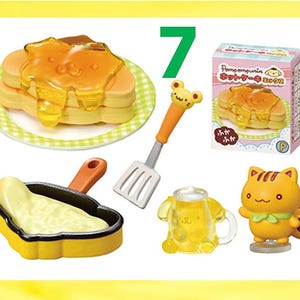 May include: A collection of miniature toy food items, including pancakes with syrup, a frying pan with a yellow substance, a spatula, a mug, and a small figurine. The items are yellow, orange, and white, with a green and white checkered plate.