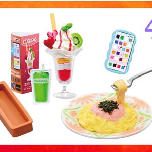 May include: A miniature set featuring a tall sundae glass with whipped cream and fruit, a green drink in a clear cup, a plate of yellow pasta with pink sauce and seaweed, a rectangular orange tray, a smartphone icon, and a pink box with Japanese text.