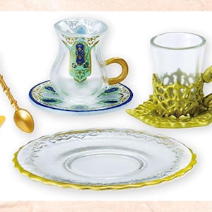 May include: A collection of decorative teacups, saucers, and a spoon. The teacups are clear with gold accents and ornate designs. The saucers are white with gold trim. A gold spoon with a turquoise accent is also included.