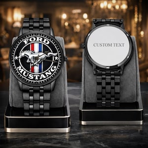 Könnte beinhalten: Zwei schwarze Armbanduhren aus Metall mit Gliederarmbändern. Die linke Uhr zeigt ein Ford Mustang-Logo mit einem laufenden Pferd, roten, weißen und blauen Streifen sowie dem Text FORD MUSTANG. Die rechte Uhr hat ein weißes Zifferblatt mit dem Text CUSTOM TEXT.