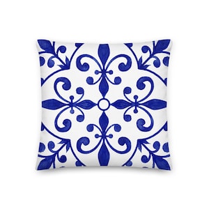 Può includere: Cuscino quadrato con sfondo bianco e motivo floreale blu ripetuto. Il design presenta fiori stilizzati simmetrici e volute in stile acquerello, creando un accento decorativo.