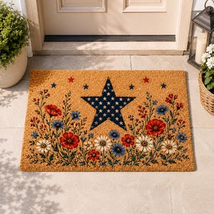 May include: A rectangular tan coir doormat featuring a large central navy blue star patterned with small white stars. The design includes a floral arrangement of red poppies, white daisies, and blue cornflowers, accented by small red and blue stars.