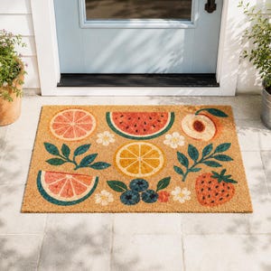 May include: A rectangular doormat with a tan background features colorful fruit illustrations. The design includes a grapefruit slice, watermelon slice, peach, orange slice, strawberry, blueberries, and white flowers. Green leaves and blue accents complete the design.