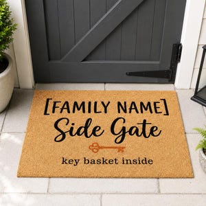 May include: A rectangular doormat made of natural coir fiber. The mat features the text "[FAMILY NAME] Side Gate" in black script, with a key graphic and the words "key basket inside" in a smaller font.