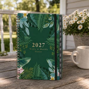 Può includere: Un'agenda settimanale e mensile 2027 con copertina verde scuro caratterizzata da una stampa botanica tropicale di foglie di palma, felci e fiori bianchi. L'agenda a spirale include una chiusura elastica nera e schede mensili nere.