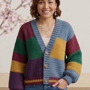May include: A multi-coloured crochet cardigan featuring panels of blue, purple, green, and yellow. The button-down sweater has a V-neck and long sleeves. The woman in the image is wearing a white vest top and a floral necklace.