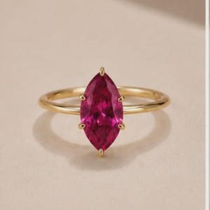 Può includere: Un anello in oro con una singola pietra preziosa rosa vivace a taglio marquise, fissata con una montatura a sei griffe. Il gambo è sottile, liscio e lucido, caratterizzato da un design essenziale che esalta la forma allungata della pietra.