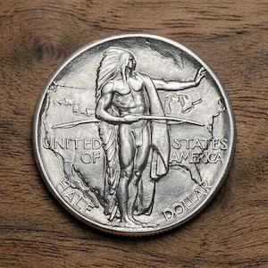 May include: A silver Half Dollar coin featuring a Native American figure with a feathered headdress and a bow. The coin is inscribed with "UNITED OF STATES AMERICA" and "HALF DOLLAR". The coin is set against a wooden background.