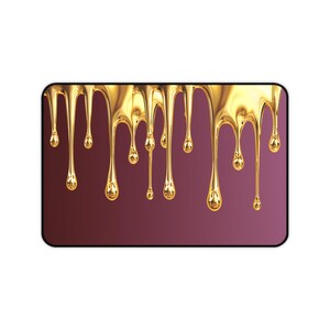 Puede incluir: Una alfombrilla de ratón rectangular con un fondo degradado marrón y morado. El diseño presenta un efecto de líquido dorado goteando, con gotas doradas que parecen derretirse sobre la superficie. La alfombrilla tiene esquinas redondeadas y un borde negro.