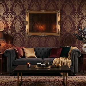May include: A luxurious living room with a dark gray tufted sofa, adorned with colorful pillows and a gold throw blanket. A dark wood coffee table holds a tea set and candle. The walls are decorated with a gold and burgundy damask pattern.