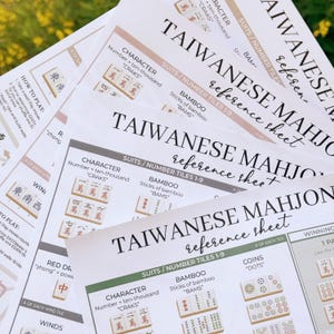 May include: A stack of white paper reference sheets titled Taiwanese Mahjong reference sheet, featuring black text and illustrations of Mahjong tiles categorized by suits, numbers, characters, bamboo, and coins, with instructions on how to play.