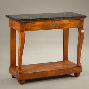 Puede incluir: Una consola de madera con una tapa de mármol gris oscuro. La mesa tiene un cajón con cerradura y patas curvas. La madera tiene un tono cálido marrón rojizo y una veta visible.