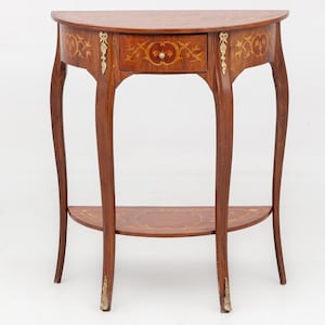 Peut inclure: Une table en bois en forme de demi-lune avec un tiroir et une étagère inférieure. La table est marron avec des motifs incrustés décoratifs et des accents dorés. Les pieds sont incurvés.