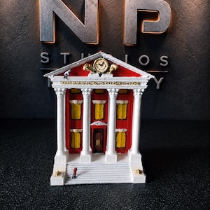 May include: A miniature model of a neoclassical building with a red facade, white columns, and yellow windows. The structure features a central clock in the pediment, a dark brown door, and a small figure standing on the front steps of the building.