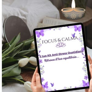 Può includere: Un tablet mostra le parole "FOCUS & CALMA" con un design floreale e a farfalla. Il testo "Il tuo Kit Anti-Stress Quotidiano" e "Ritrova il tuo equilibrio..." sono anch'essi visibili. Il tablet è tenuto in mano, con tulipani bianchi e una candela accesa sullo sfondo.