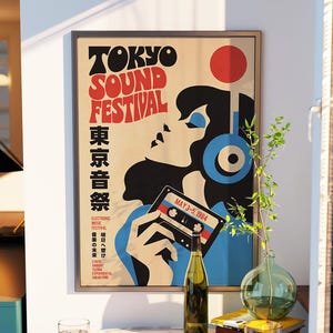 May include: A framed poster titled Tokyo Sound Festival featuring a stylized illustration of a person wearing blue headphones and holding a cassette tape labeled May 3-5, 1984, with bold red and black typography against a cream background.