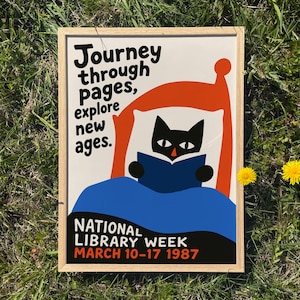 May include: A framed poster with a whimsical illustration of a black cat reading a book in a chair. The poster has the text "Journey through pages, explore new ages." and "National Library Week March 10-17 1987."