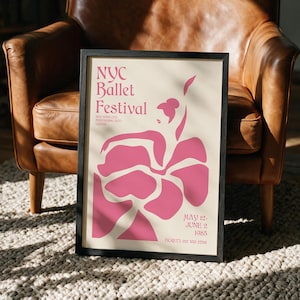 Puede incluir: Un póster enmarcado con fondo crema y formas abstractas rosas que representan a una persona bailando. El texto dice: NYC Ballet Festival, New York City Performing Arts Center, May 12-June 2 1985, y Tickets 212 555 2788. El marco es negro y rectangular.