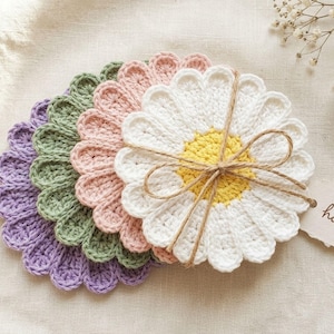 May include: A stack of handmade crochet daisy coasters in various pastel colors: purple, green, pink, and white with a yellow center. Tied with twine and a small tag that says "handmade".