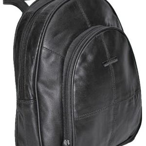 May include: A black leather backpack featuring a rounded top silhouette, multiple zippered compartments, and a small rectangular metal logo plate on the front pocket. The bag includes a top carry handle and visible stitched paneling details.